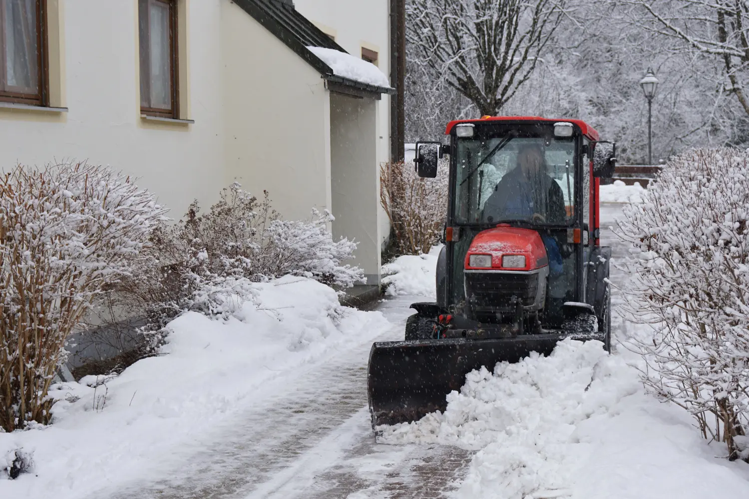 Räumdienst, Traktor mit Schneepflug auf Gehweg vor Haus